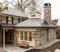 a stone house with a metal roof and two benches on the front porch, along with brick chimneys