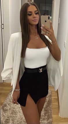 a woman taking a selfie while wearing a white top and black high waist shorts