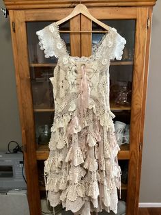 a dress hanging on a wooden hanger in front of a glass case filled with dishes