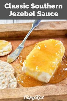 a wooden cutting board topped with crackers and cheese on top of it next to a spoon