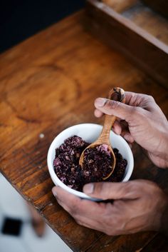 two hands holding a white bowl filled with blueberry compote on top of a wooden table