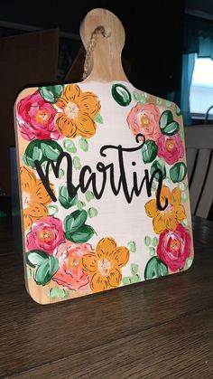 a wooden cutting board with flowers painted on it and the word martin written in black