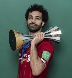 a man holding two trophies in front of his face and wearing a red shirt with gold trim