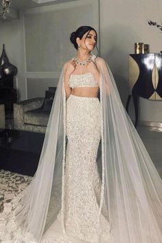 a woman in a white wedding dress with a veil on her head, standing next to a chandelier