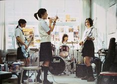 some girls are playing instruments and singing in a room with other young people standing around