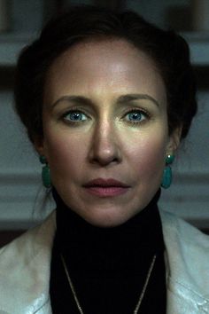 a woman with blue eyes wearing green earrings and a black turtle neck sweater is looking at the camera