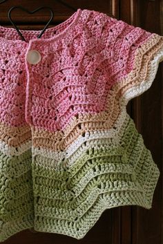 a pink and green crocheted sweater hanging from a hook on a wooden door