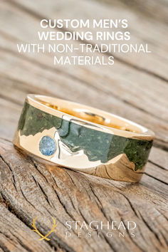 a gold wedding ring with green and blue flowers on it, sitting on top of a wooden