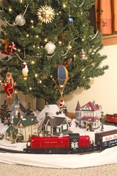 a christmas tree is decorated with ornaments and train tracks in front of a small town