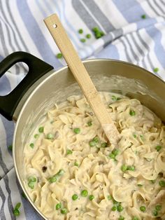 a pot filled with pasta and peas on top of a blue striped table cloth next to a wooden spoon