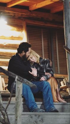 a man and woman sitting on the porch of a log cabin with their arms around each other