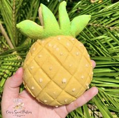 a hand holding a small yellow pineapple shaped toy in front of a palm tree