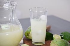 a pitcher and glass filled with lemonade next to limes on a cutting board