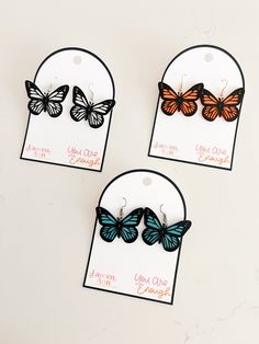 three butterfly shaped earrings are shown on a white card with black and orange butterflies hanging from them