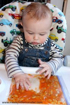 a baby sitting in a high chair eating food from a bowl with his hands on the tray