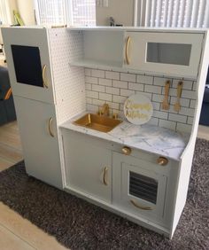 a toy kitchen with white cabinets and marble counter tops, gold handles on the doors