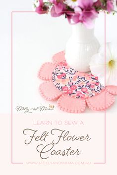 a white vase filled with pink flowers next to a flower pot and some felt coasters