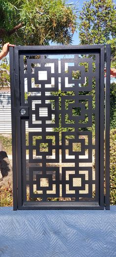 a metal gate with an intricate design on the top and bottom, in front of some trees