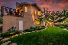 an exterior view of a home at dusk with green grass and trees in the foreground