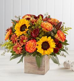 an arrangement of sunflowers and other flowers in a wooden vase on a table