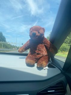 a brown teddy bear sitting on the dashboard of a car