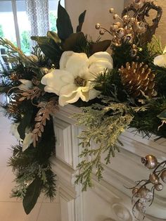 a fireplace mantel decorated with white flowers and greenery, pine cones and silver bells