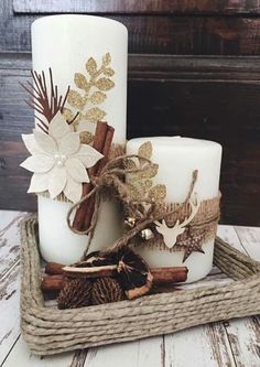 two white candles sitting on top of a tray next to pine cones and cinnamons