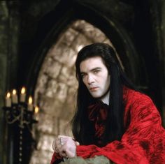 a man with long black hair wearing a red robe and holding a knife in his hand