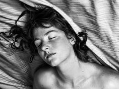 a black and white photo of a woman laying in bed with her head on the pillow