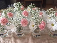 pink and white flowers are in glass vases on a tablecloth covered table cloth