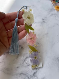 a hand holding a piece of glass with flowers on it and a tassel hanging from the end