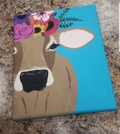 a painting of a cow with flowers on it's head sitting on a counter