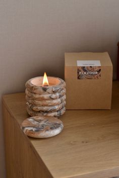 a lit candle sitting on top of a wooden table next to a box and some cookies