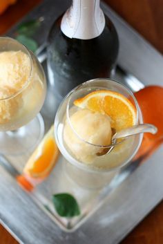 two glasses filled with ice cream and orange slices on a tray next to a bottle