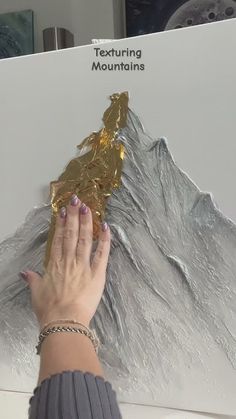 a woman holding onto a piece of gold foil in front of a mountain range sign