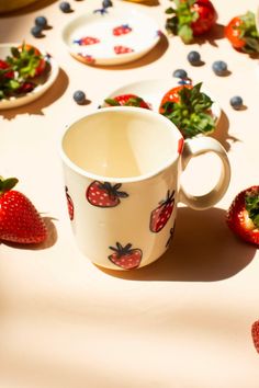 strawberries and blueberries are scattered around a coffee cup on a table with plates