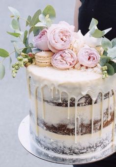 a person holding a cake with flowers on top and icing drizzled over it