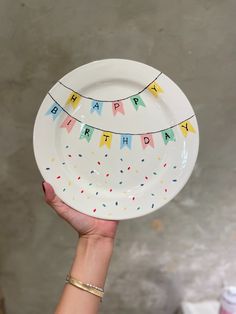 a hand holding a happy birthday plate with streamers