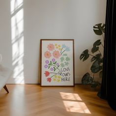 a white chair sitting in front of a framed flower print on the floor next to a plant