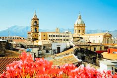 the city is full of tall buildings and colorful flowers in front of them, with mountains in the background