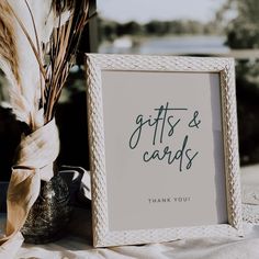 a white frame sitting on top of a table next to a vase filled with flowers