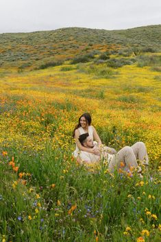 two women sitting in a field full of wildflowers and grass, one holding a baby