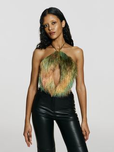 a woman in black leather pants and a crop top with feathers on the back, posing for