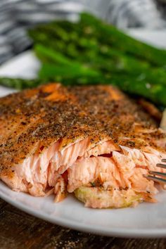 a white plate topped with salmon and asparagus on top of a wooden table