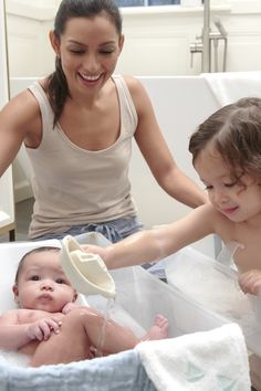 a woman washes her baby in the bathtub while another plays with it's hair