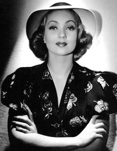 a black and white photo of a woman wearing a hat with her arms crossed in front of her chest