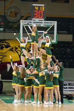 a group of cheerleaders standing on top of each other in front of a basketball court