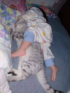 a small child laying on top of a bed next to a gray and white cat