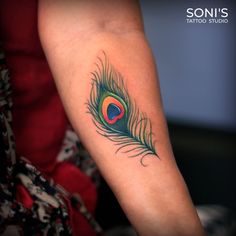 a colorful peacock feather tattoo on the arm