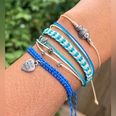 four bracelets with charms on the arm, one blue and one white braided cord